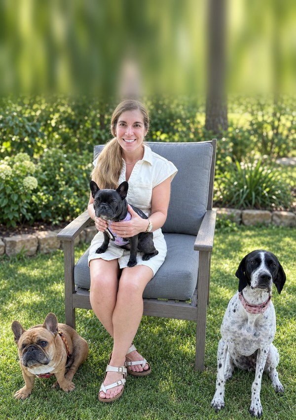 Dr. Kristin Wrycha sitting in a garden chair with a black French Bulldog on her lap and her dogs beside her.